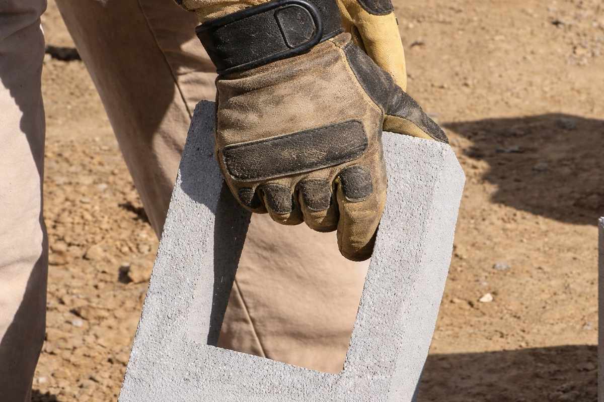 Pohabane radne rukavice koje drže betonski blok, primer neodržavane zaštitne opreme u građevinskim uslovima.