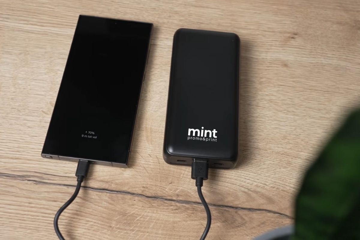 Pametni telefon povezan na punjač i power bank na radnom stolu u kancelariji